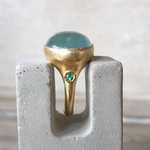 May include: A gold ring with a large, light blue gemstone and a smaller, green gemstone set in the band.
