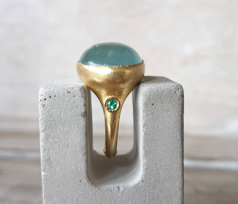May include: A gold ring with a large, light blue gemstone and a smaller, green gemstone set in the band.