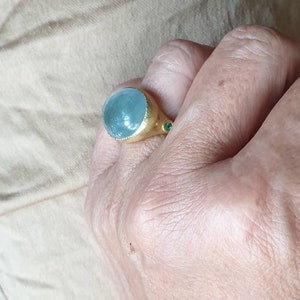 May include: A gold ring with a large, round, light blue gemstone and two smaller, green gemstones on the band.