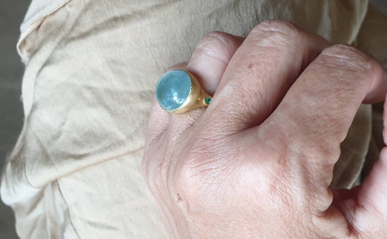 May include: A gold ring with a large, round, light blue gemstone and two smaller, green gemstones on the band.