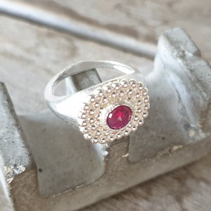 May include: A silver ring with a red gemstone set in a circle of small silver beads.