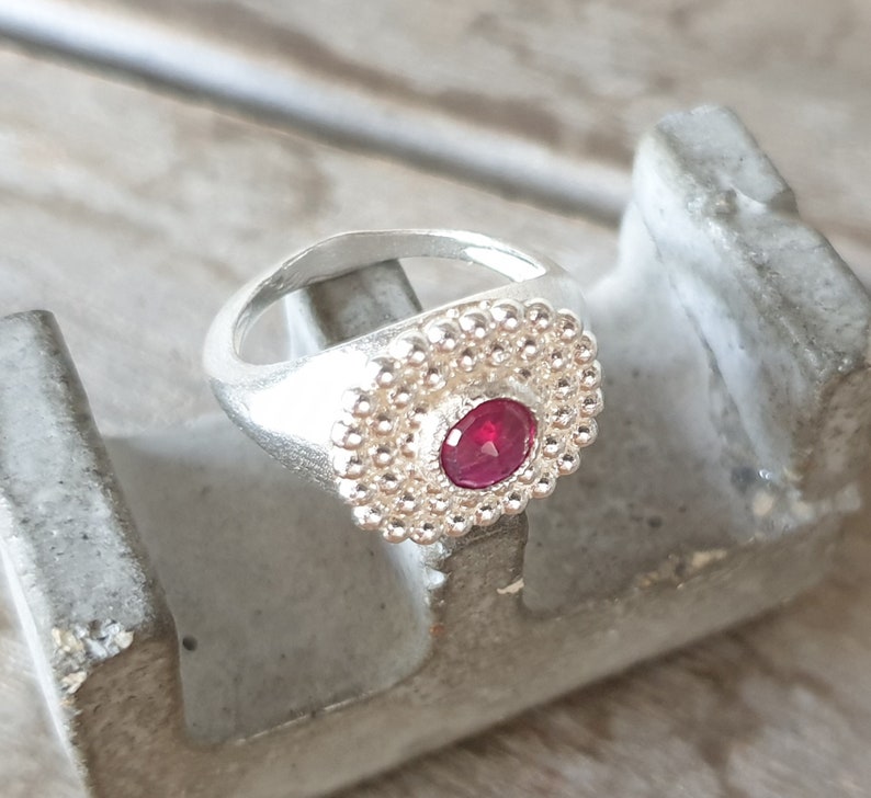 May include: A silver ring with a red gemstone set in a circle of small silver beads.