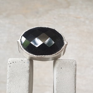 May include: A silver ring with a black faceted gemstone set in a bezel setting.