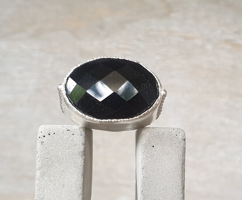May include: A silver ring with a black faceted gemstone set in a bezel setting.