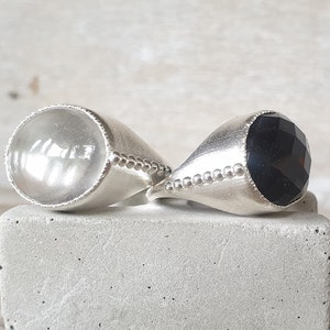 May include: Two silver rings with a clear and black gemstone. The rings have a beaded edge.