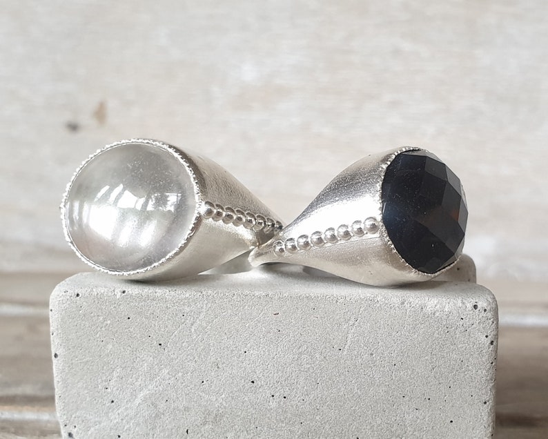 May include: Two silver rings with a clear and black gemstone. The rings have a beaded edge.