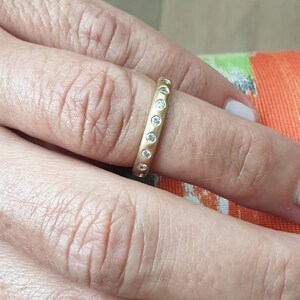 Peut inclure: Une bague dor&eacute;e orn&eacute;e de petits pierres pr&eacute;cieuses transparentes serties autour de l'anneau. La bague est port&eacute;e au doigt, mettant en valeur son design simple mais &eacute;l&eacute;gant. Les pierres sont espac&eacute;es uniform&eacute;ment.