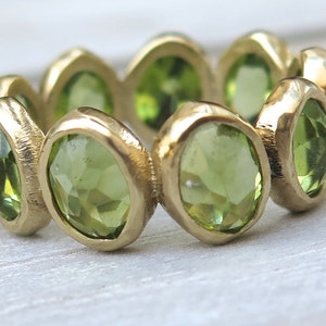 May include: A gold ring with a band of green gemstones. The ring is set with multiple oval-shaped stones.