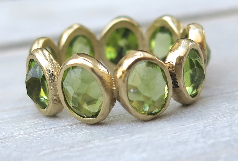 May include: A gold ring with a band of green gemstones. The ring is set with multiple oval-shaped stones.