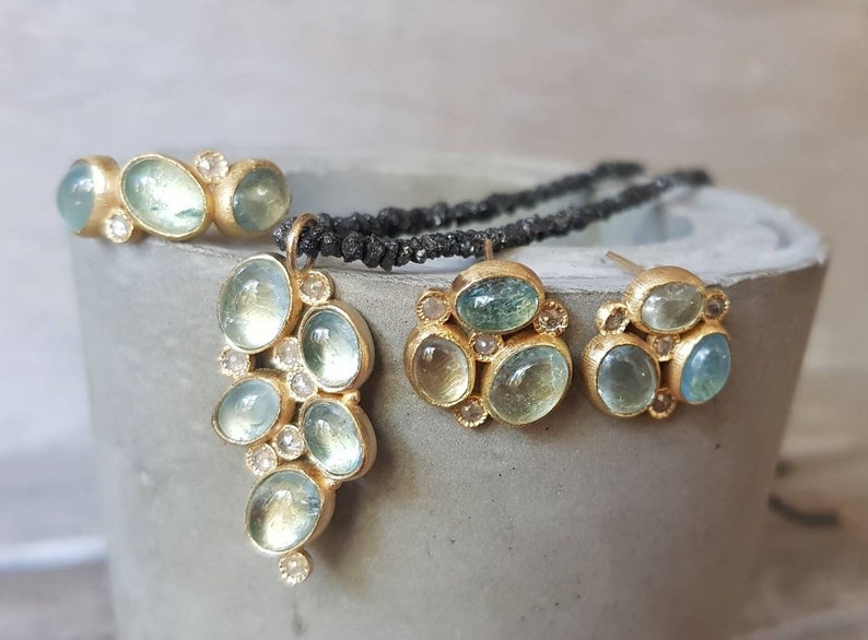 Pu&ograve; includere: Un set di gioielli in pietra di acquamarina composto da una collana con ciondolo, un anello e un paio di orecchini. I gioielli sono in oro e presentano piccoli diamanti rotondi.