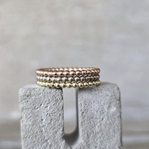 Puede incluir: Cuatro anillos apilados hechos de pequeñas cuentas. Los anillos son de tres colores diferentes: oro rosa, plata y oro.