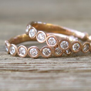 May include: Two rose gold bands with bezel set round diamonds. The bands are stacked on top of each other.