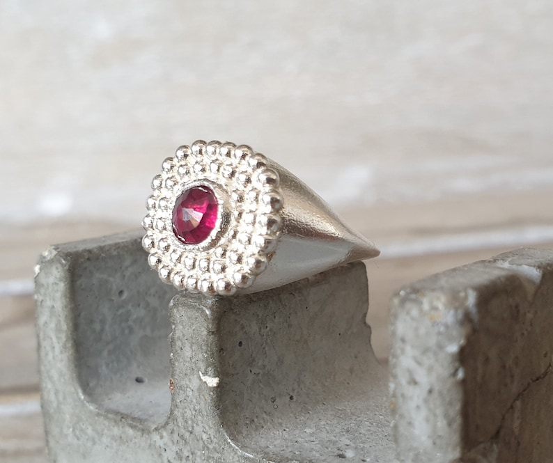 May include: A silver ring with a textured band and a single red gemstone in the center.