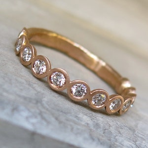 May include: A rose gold band ring with a row of bezel-set round diamonds.