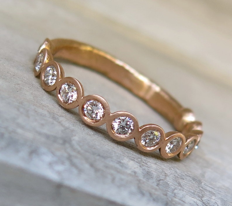 May include: A rose gold band ring with a row of bezel-set round diamonds.