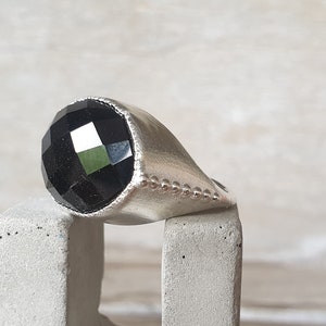 May include: A silver ring with a black faceted gemstone. The ring has a beaded edge.