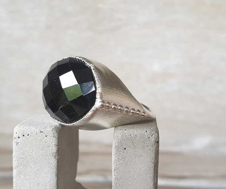 May include: A silver ring with a black faceted gemstone. The ring has a beaded edge.