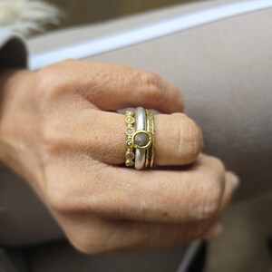 Pu&ograve; includere: Un set di tre anelli in oro e argento con un solo diamante rotondo nell'anello centrale. Gli anelli sono impilati su un dito.