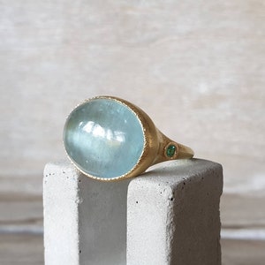 May include: A gold ring with a large oval aquamarine gemstone and a small green gemstone accent.