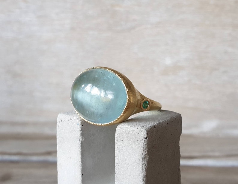 May include: A gold ring with a large oval aquamarine gemstone and a small green gemstone accent.