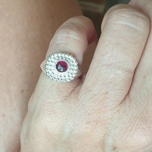 May include: A silver ring with a red gemstone set in a circular design.
