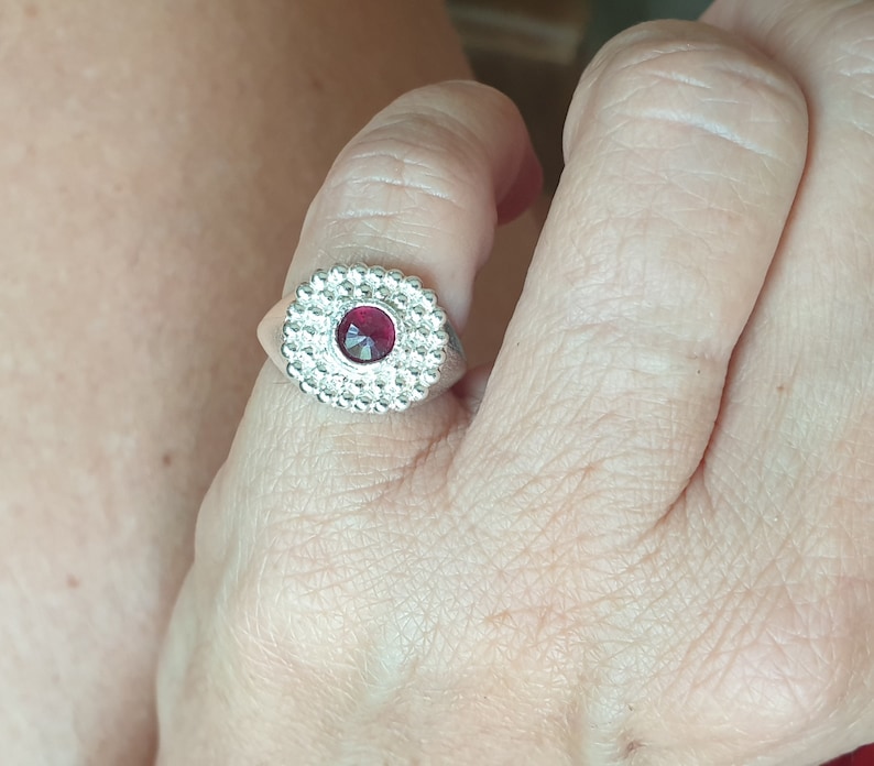May include: A silver ring with a red gemstone set in a circular design.