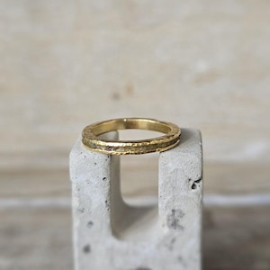 Pu&ograve; includere: Un anello a fascia d'oro con una texture martellata e una sottile fila di piccoli diamanti incastonati nella fascia.