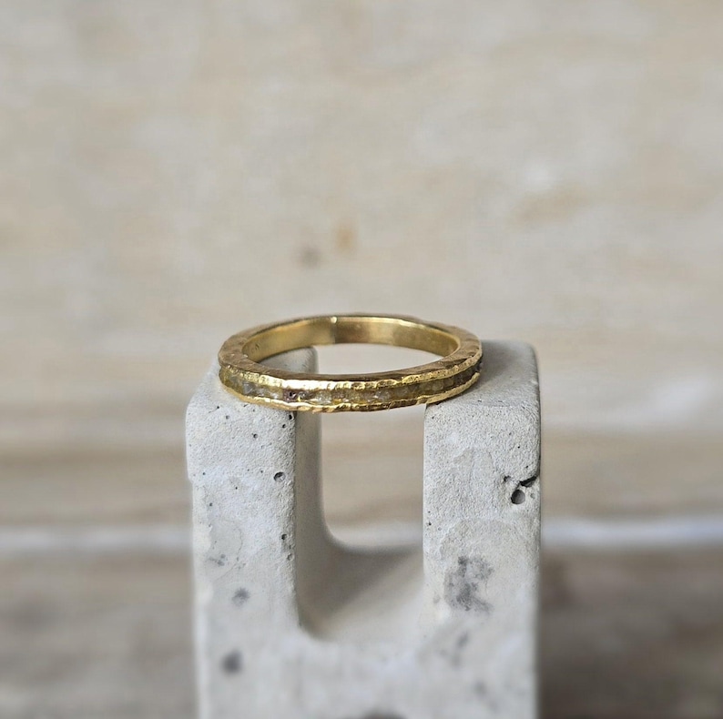 Pu&ograve; includere: Un anello a fascia d'oro con una texture martellata e una sottile fila di piccoli diamanti incastonati nella fascia.