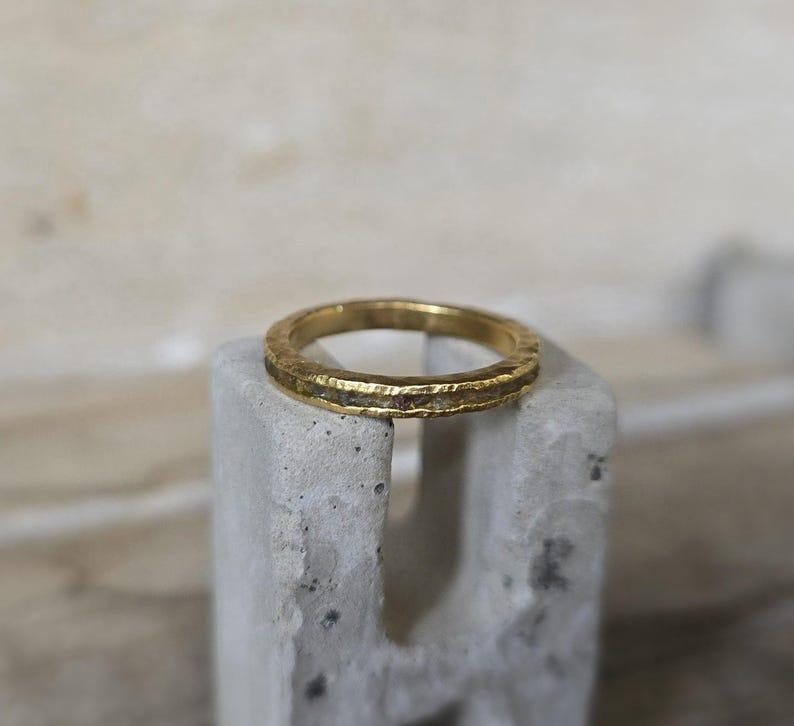 Pu&ograve; includere: Un anello a fascia d'oro con una superficie testurizzata e una sottile linea di pietre bianche attorno al bordo.
