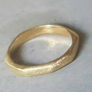May include: A gold ring with a textured, irregular, and slightly uneven surface. The ring is made of a thick band of metal.