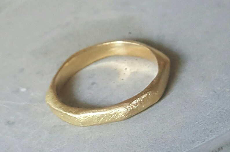 May include: A gold ring with a textured, irregular, and slightly uneven surface. The ring is made of a thick band of metal.