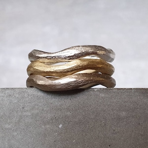 Può includere: Un anello a tre bande in argento e oro. Le bande sono ondulate e hanno una finitura testurizzata.
