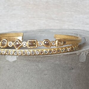 May include: Two gold bracelets with a row of small diamonds and a row of larger, irregularly shaped diamonds.