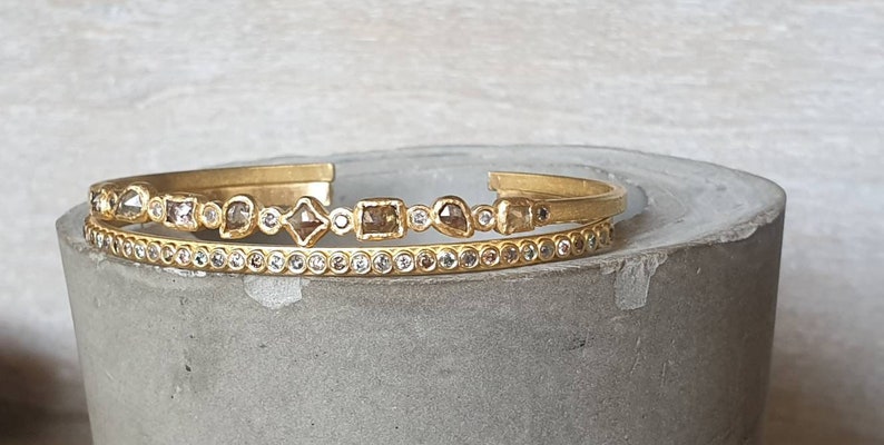 May include: Two gold bracelets with a row of small diamonds and a row of larger, irregularly shaped diamonds.