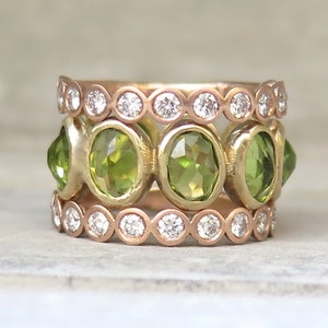 May include: A gold ring with three bands. The top and bottom bands are set with small round diamonds. The middle band is set with five oval green gemstones.