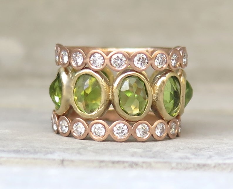 May include: A gold ring with three bands. The top and bottom bands are set with small round diamonds. The middle band is set with five oval green gemstones.