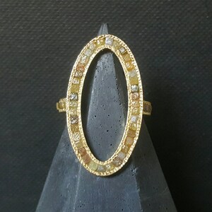 May include: A gold ring with an oval-shaped setting. The setting is filled with small, colorful diamonds.