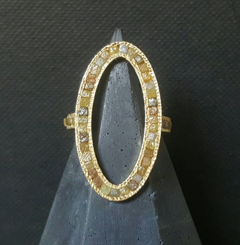 May include: A gold ring with an oval-shaped setting. The setting is filled with small, colorful diamonds.
