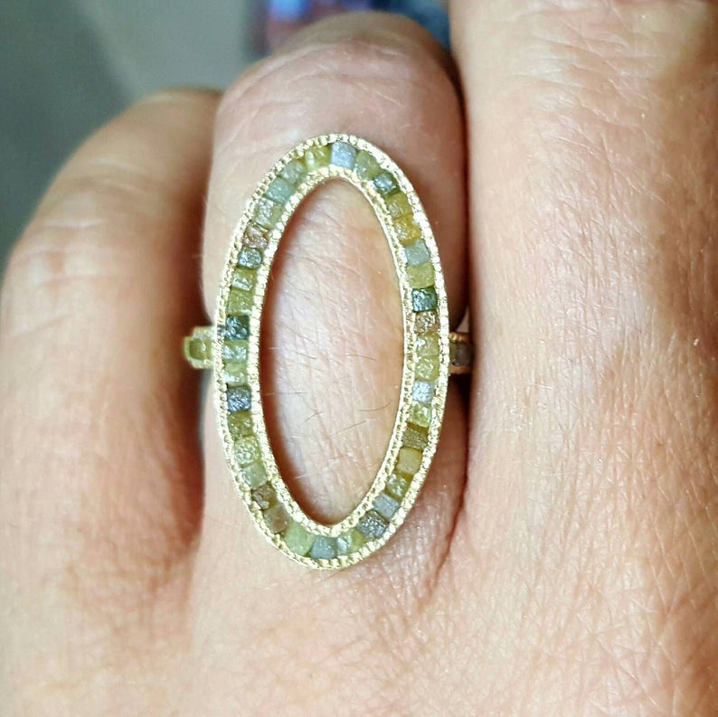 May include: A gold ring with an oval-shaped setting. The setting is filled with small, colorful diamonds.
