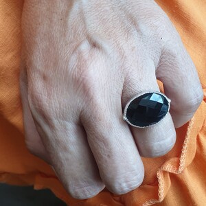 May include: A silver ring with a large, faceted black gemstone. The ring is worn on a person's finger.