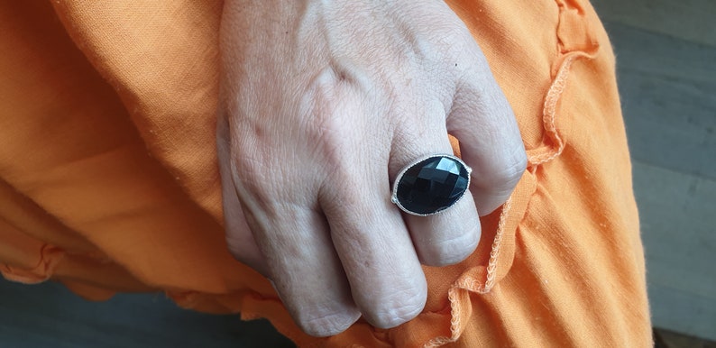 May include: A silver ring with a large, faceted black gemstone. The ring is worn on a person's finger.
