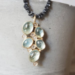 Pu&ograve; includere: Una collana con un ciondolo in oro composto da un gruppo di pietre di acquamarina blu chiaro e piccoli diamanti trasparenti. La collana &egrave; realizzata con perline nere.