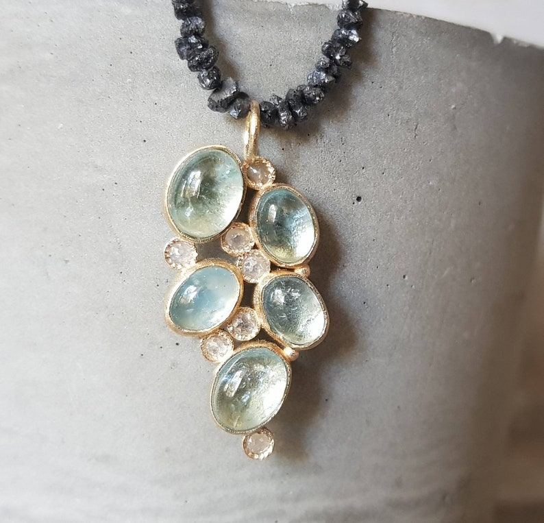 Pu&ograve; includere: Una collana con un ciondolo in oro composto da un gruppo di pietre di acquamarina blu chiaro e piccoli diamanti trasparenti. La collana &egrave; realizzata con perline nere.