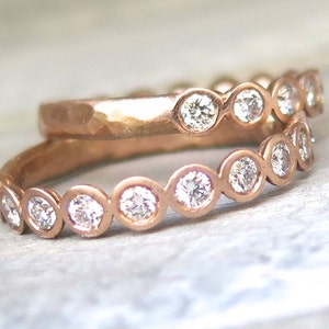May include: Two rose gold bands with bezel set round diamonds. The top band is hammered and the bottom band has a wavy design.