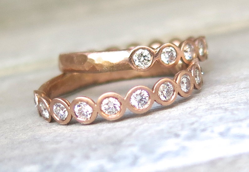 May include: Two rose gold bands with bezel set round diamonds. The top band is hammered and the bottom band has a wavy design.