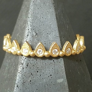 Può includere: Un anello d'oro con una fila di accenti a forma di lacrima incastonati con piccole pietre trasparenti.