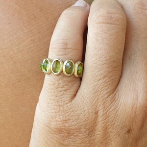 May include: A gold ring with five oval-shaped green gemstones set in a band.