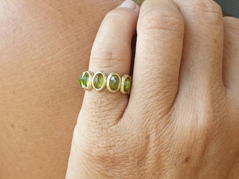 May include: A gold ring with five oval-shaped green gemstones set in a band.