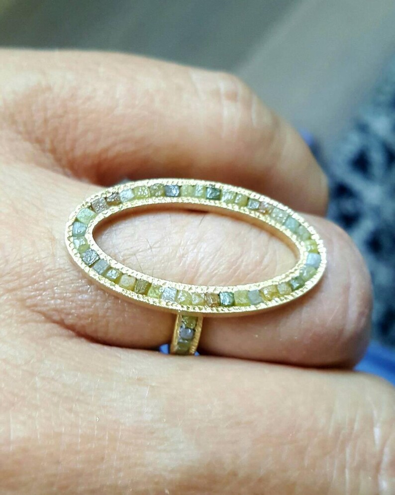 May include: A gold ring with a large oval-shaped setting. The setting is filled with small, green, and gray diamonds.