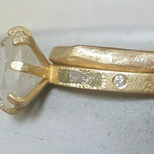 May include: A gold ring with a large, clear gemstone set in a prong setting. The ring is paired with a matching band with a smaller diamond accent.